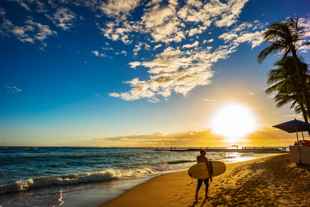 Photo of a person holding a surf board on the beach ready for a day of Maui water sports