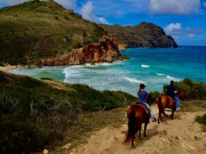Photo of two people horseback riding on Maui with mountain and ocean views